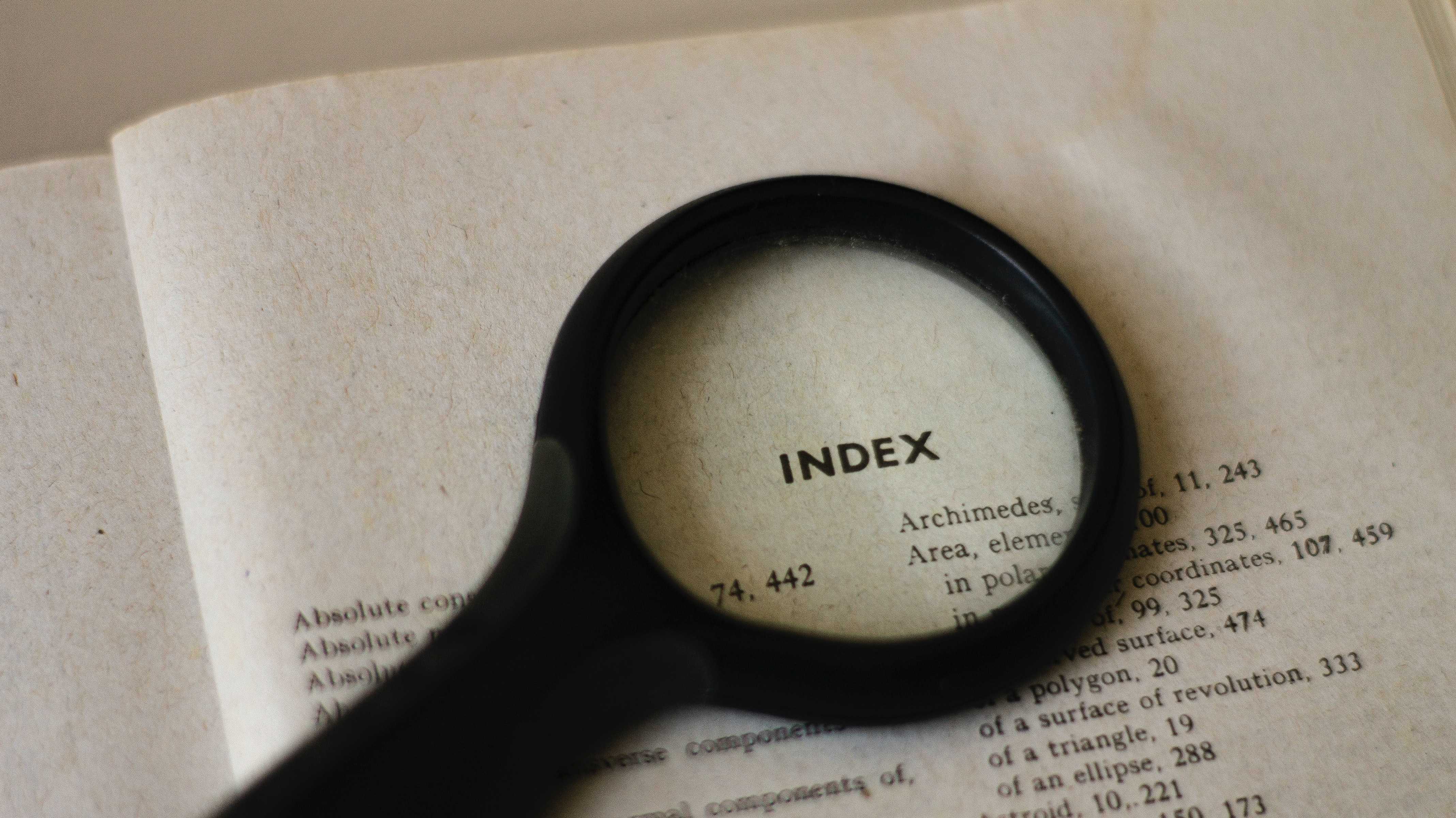 A magnifying glass on a book, placed over the word 'Index'