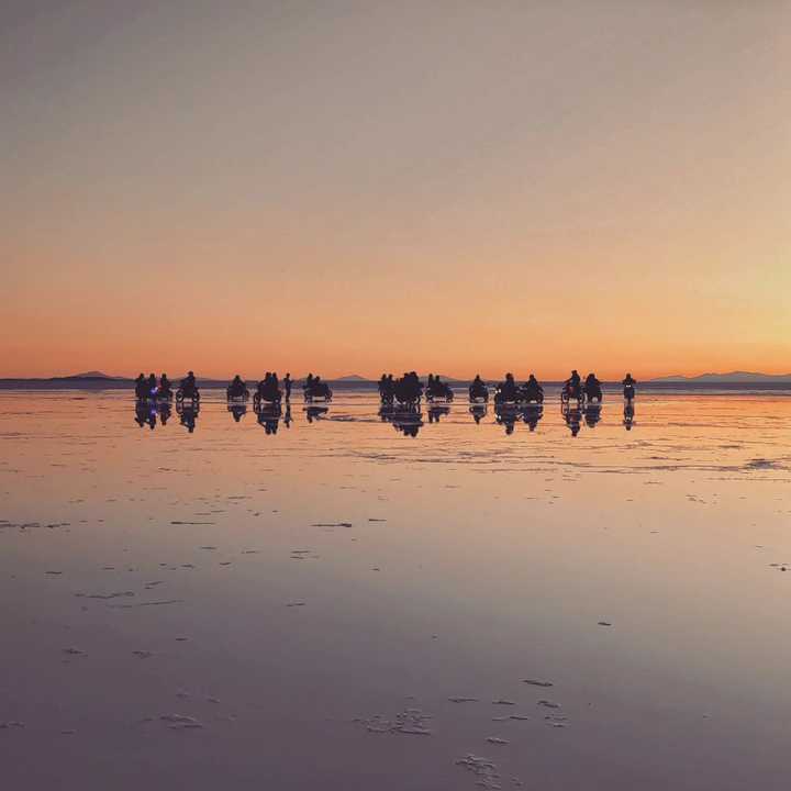 Motorcyclists reflected on the watery surface of the Uyuni Salt Flats during sunset.
